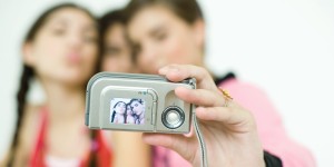 Three young female friends taking photo of selves with digital camera, focus on camera in foreground