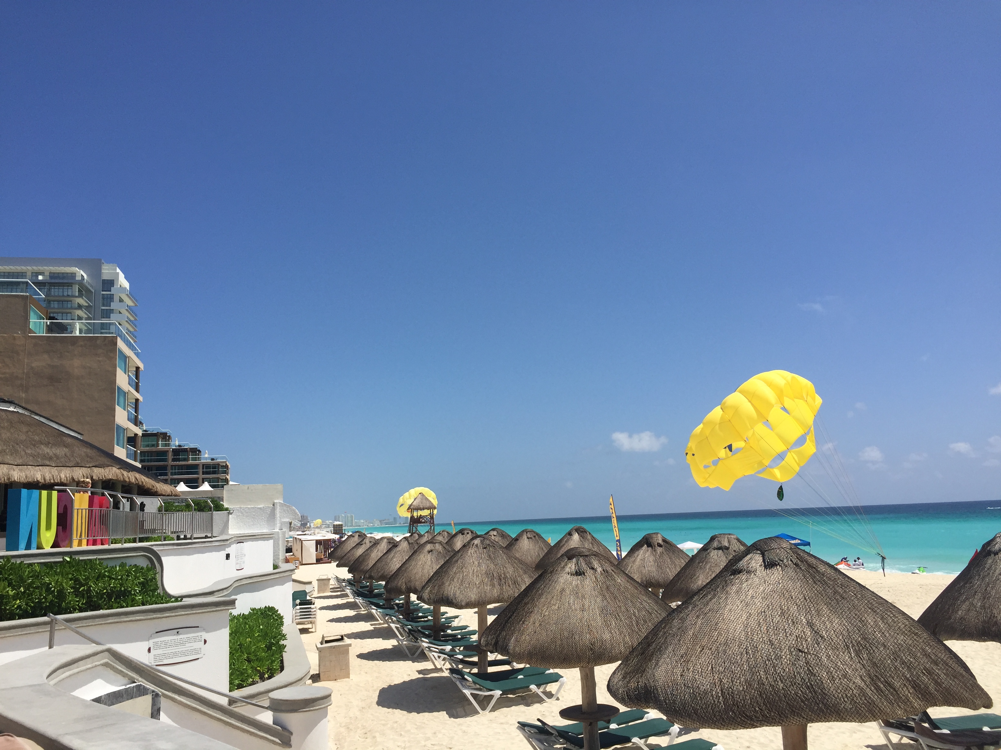Beach loungers with parasols and a parasailer in clear blue skies.