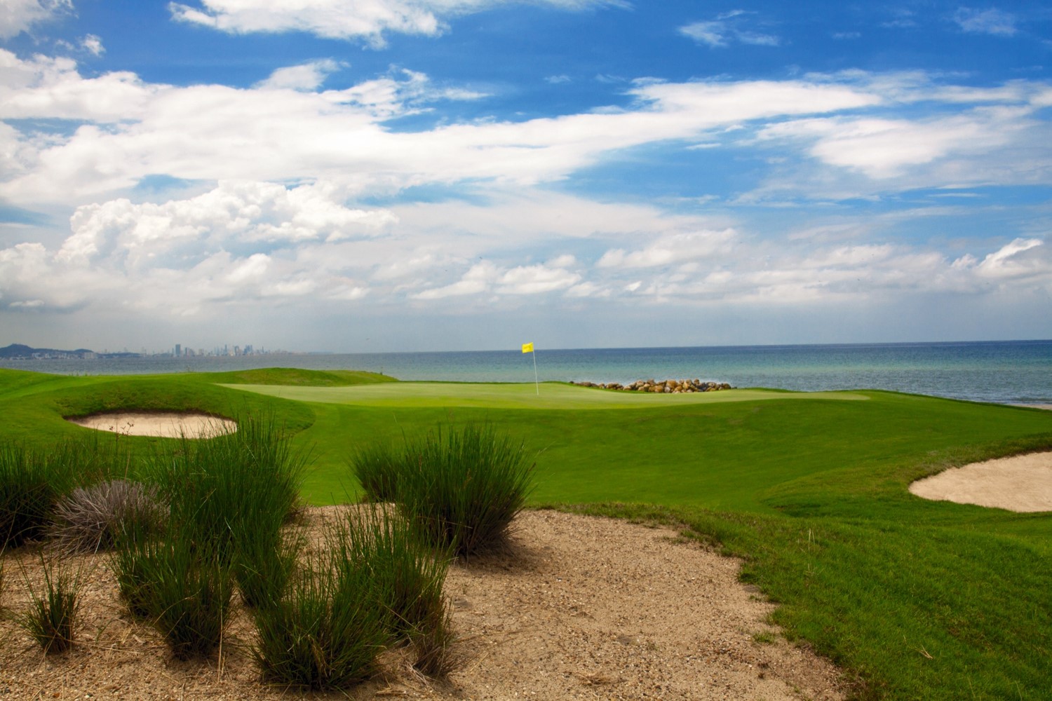 A serene golf course by the ocean under a blue sky.