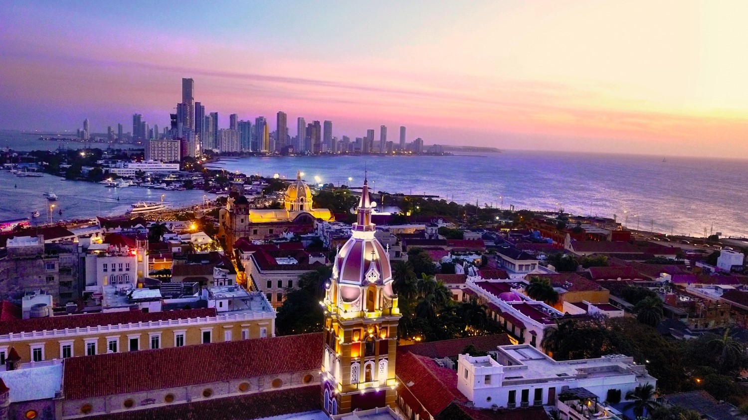 Sunset over a vibrant city skyline with historic architecture and a waterfront.