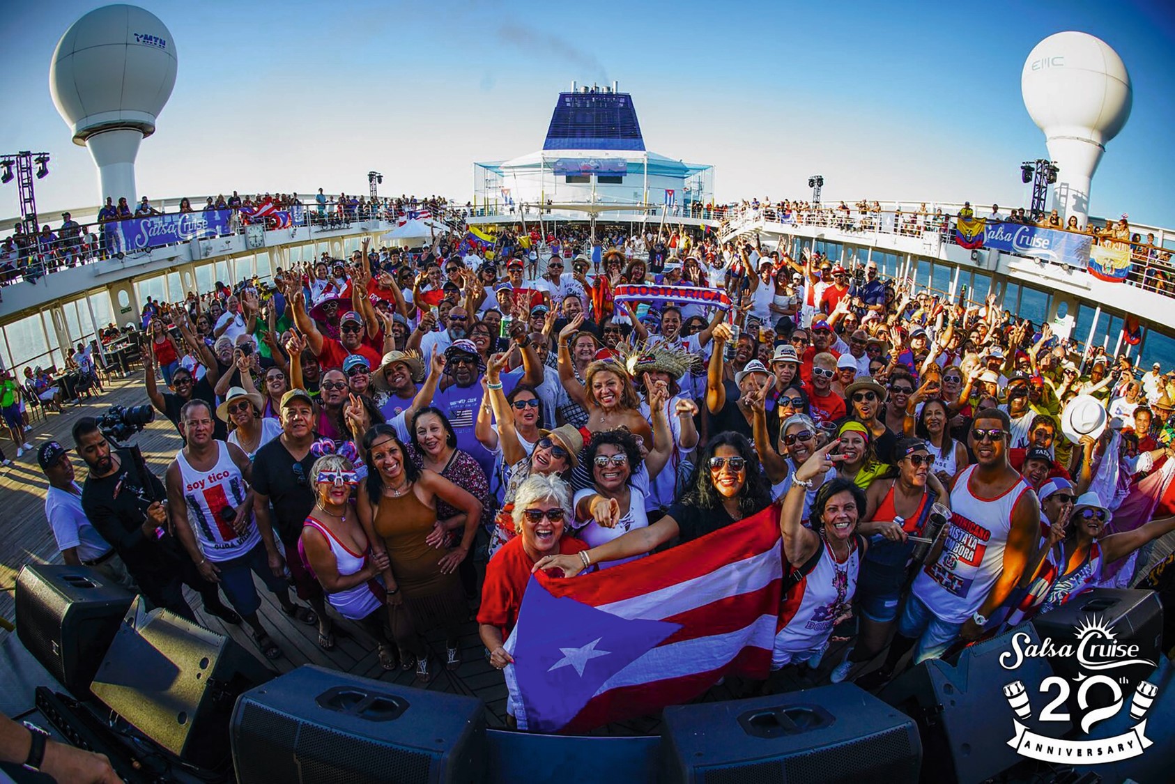 Crowd enjoying a lively event on a cruise ship deck, waving a Puerto Rican flag.