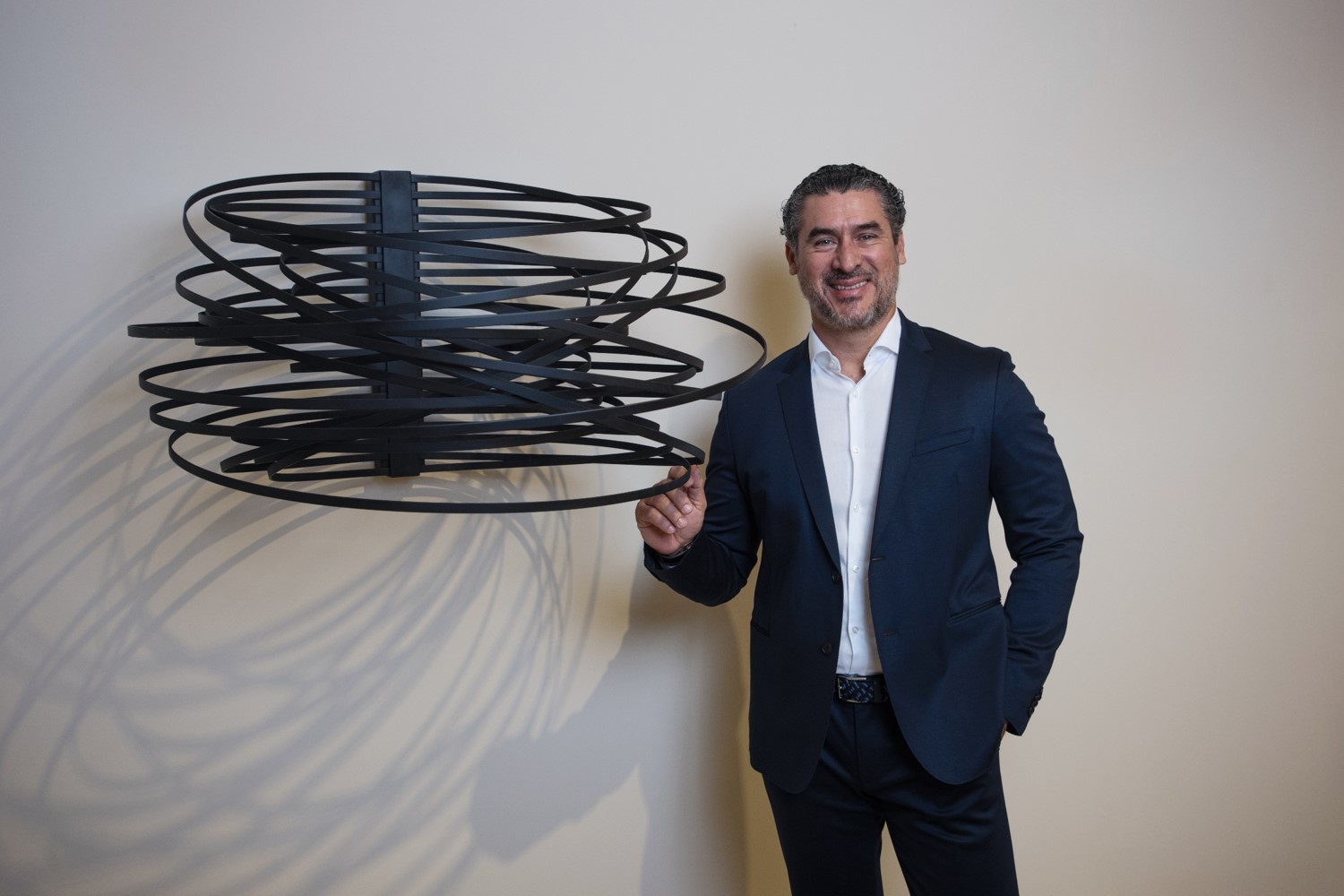 Man in suit posing with modern circular sculpture on wall.