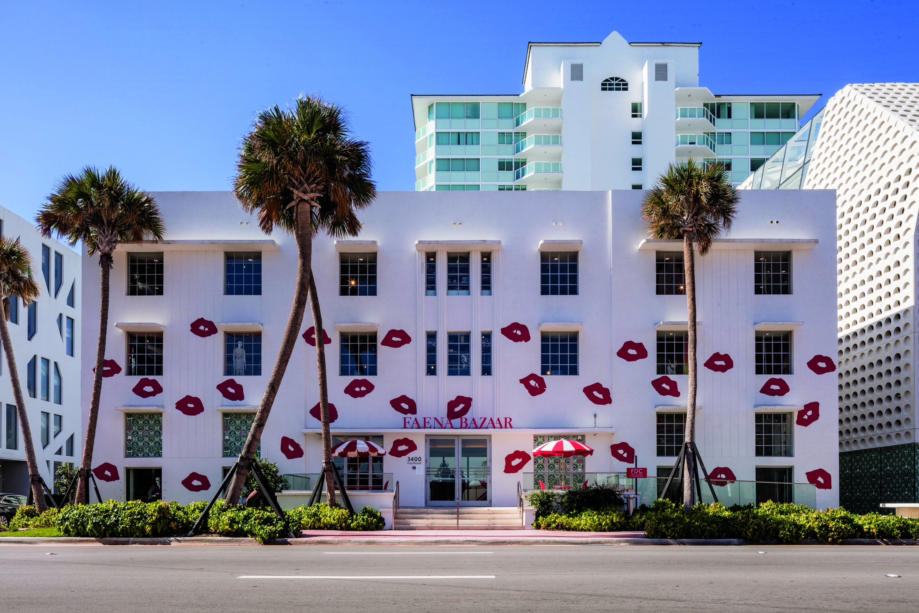 White building decorated with red lips and palm trees in front.