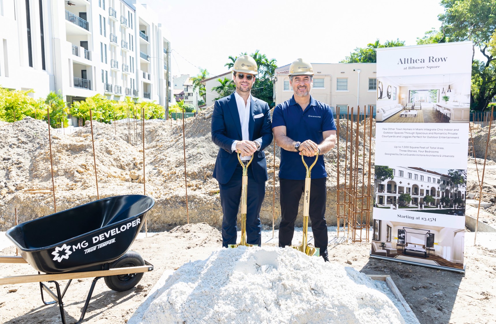 Two men in suits and hard hats at a groundbreaking ceremony.