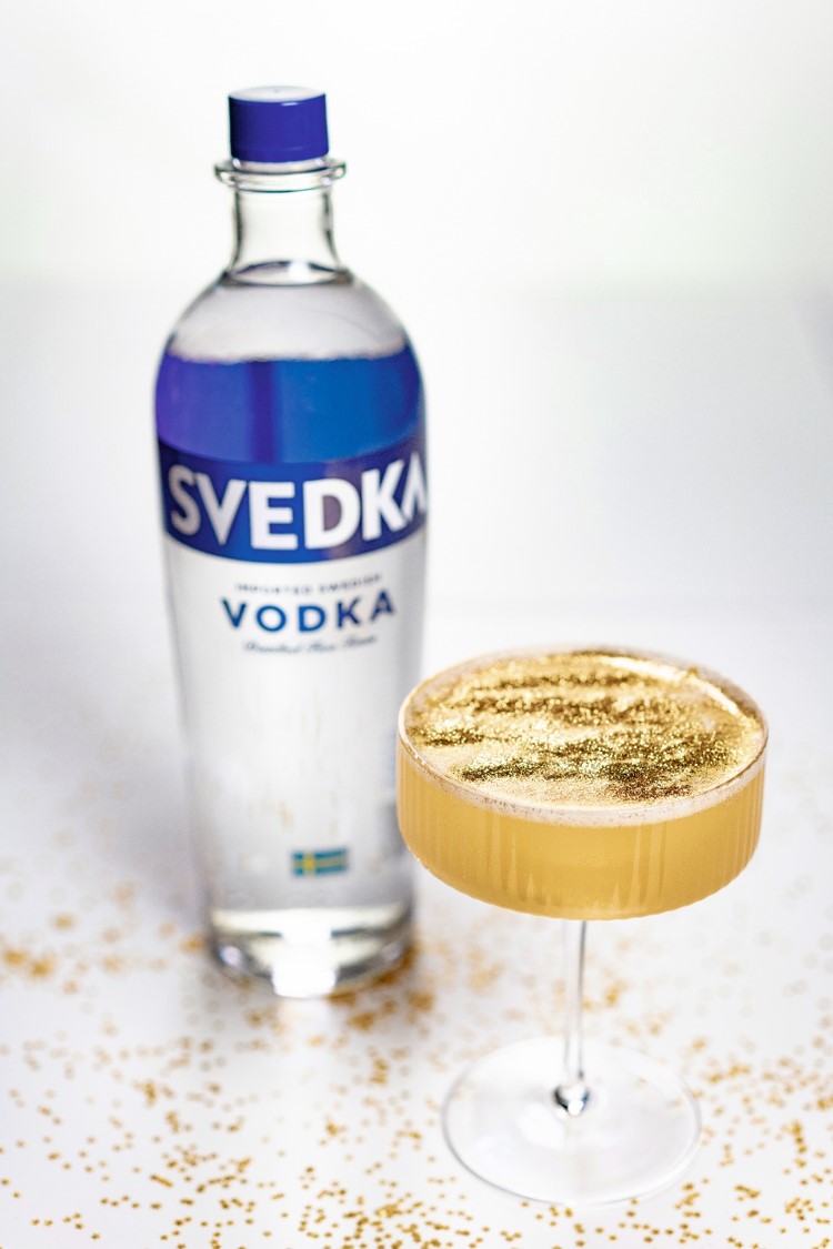 A bottle of Svedka vodka with a creamy cocktail topped with nutmeg.