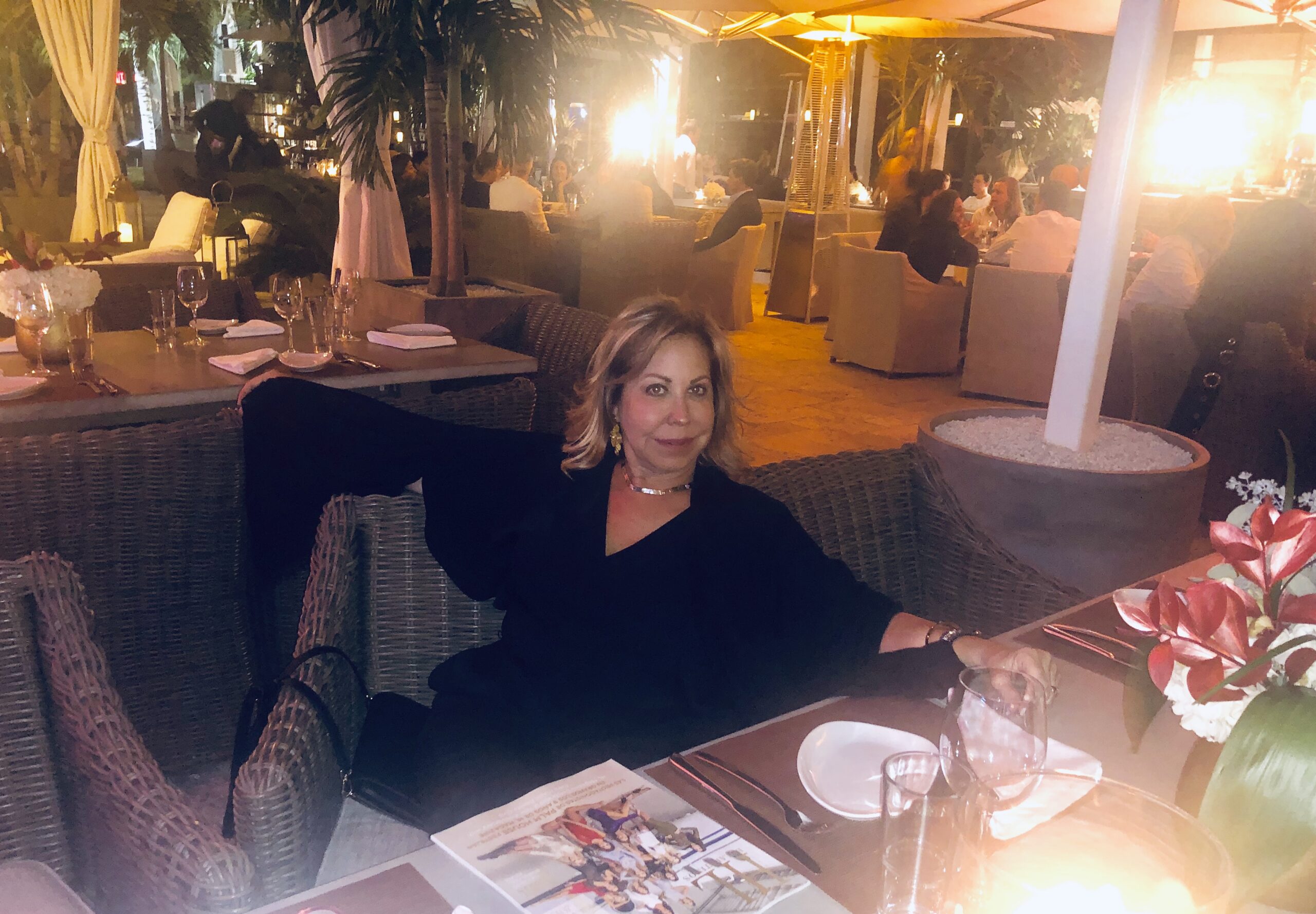 Woman in black seated at a softly lit outdoor restaurant at night.