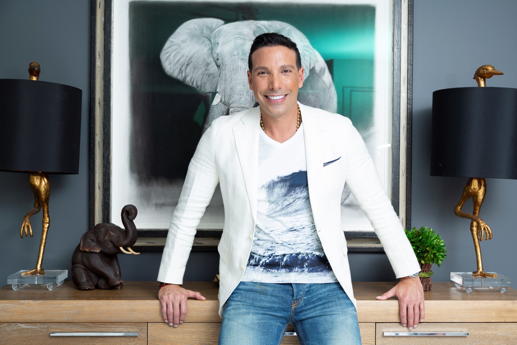 A man in a white blazer smiles, standing in front of an elephant photo.