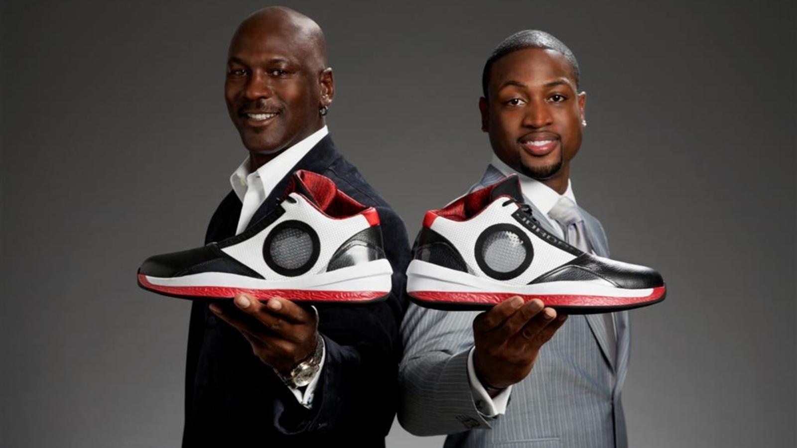 Two men holding oversized sneakers and smiling.