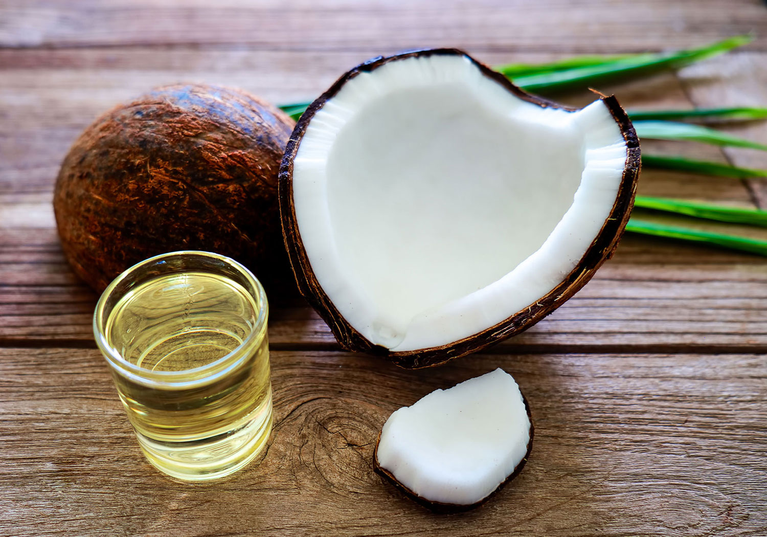 A fresh coconut with a glass of coconut oil on a wooden surface.