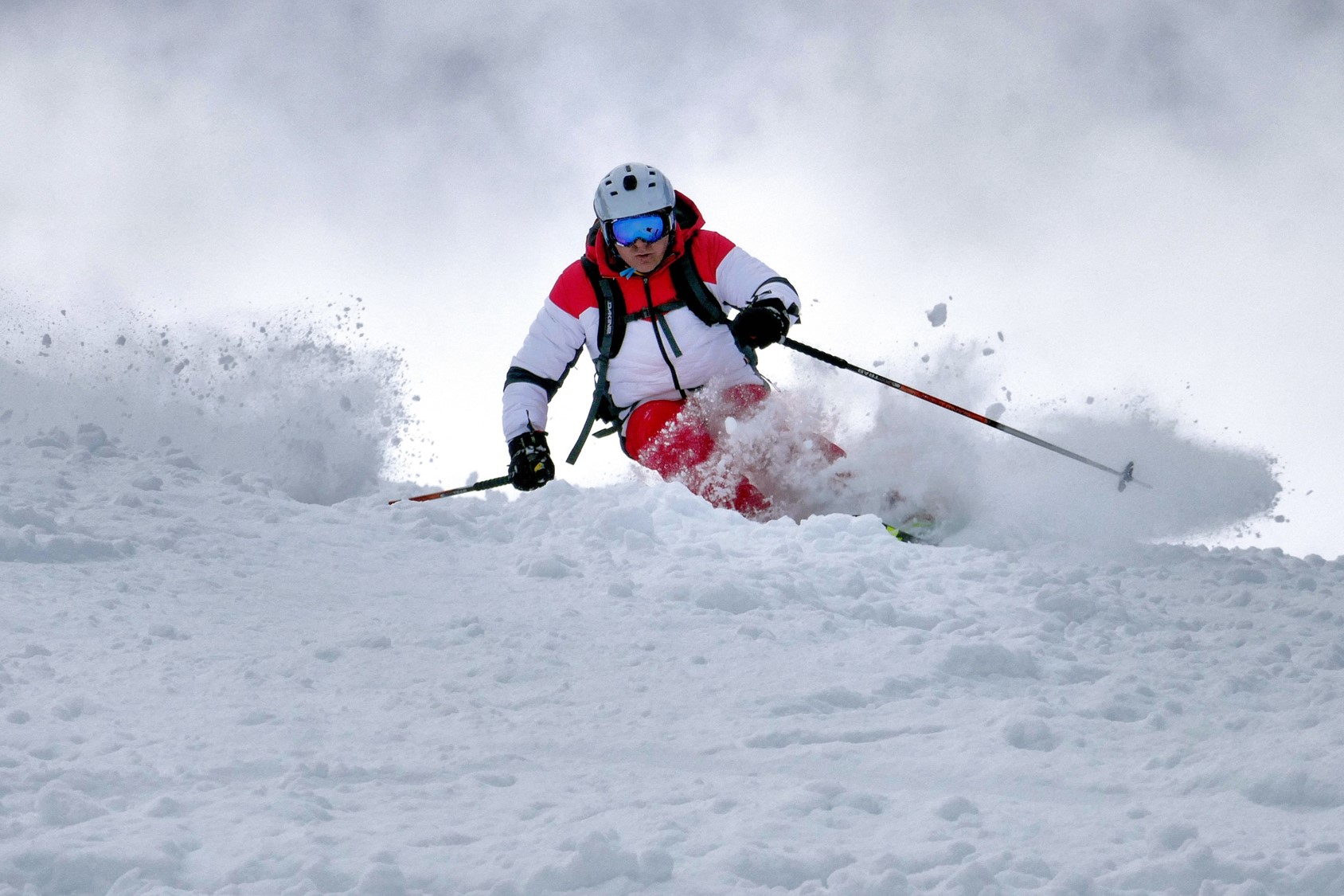 Skier carving through fresh snow on a cloudy day.