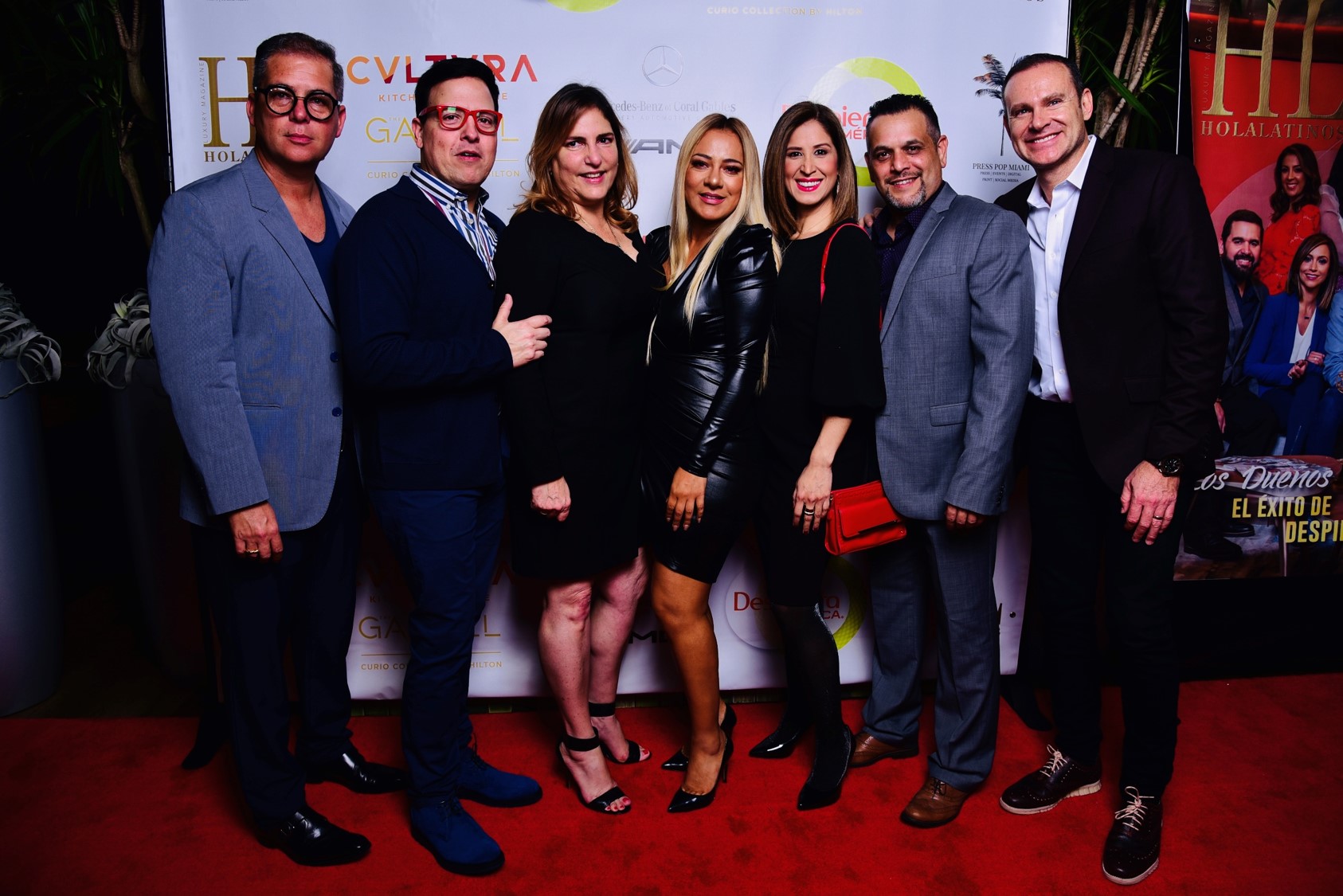 Group of seven people posing on a red carpet at an event.