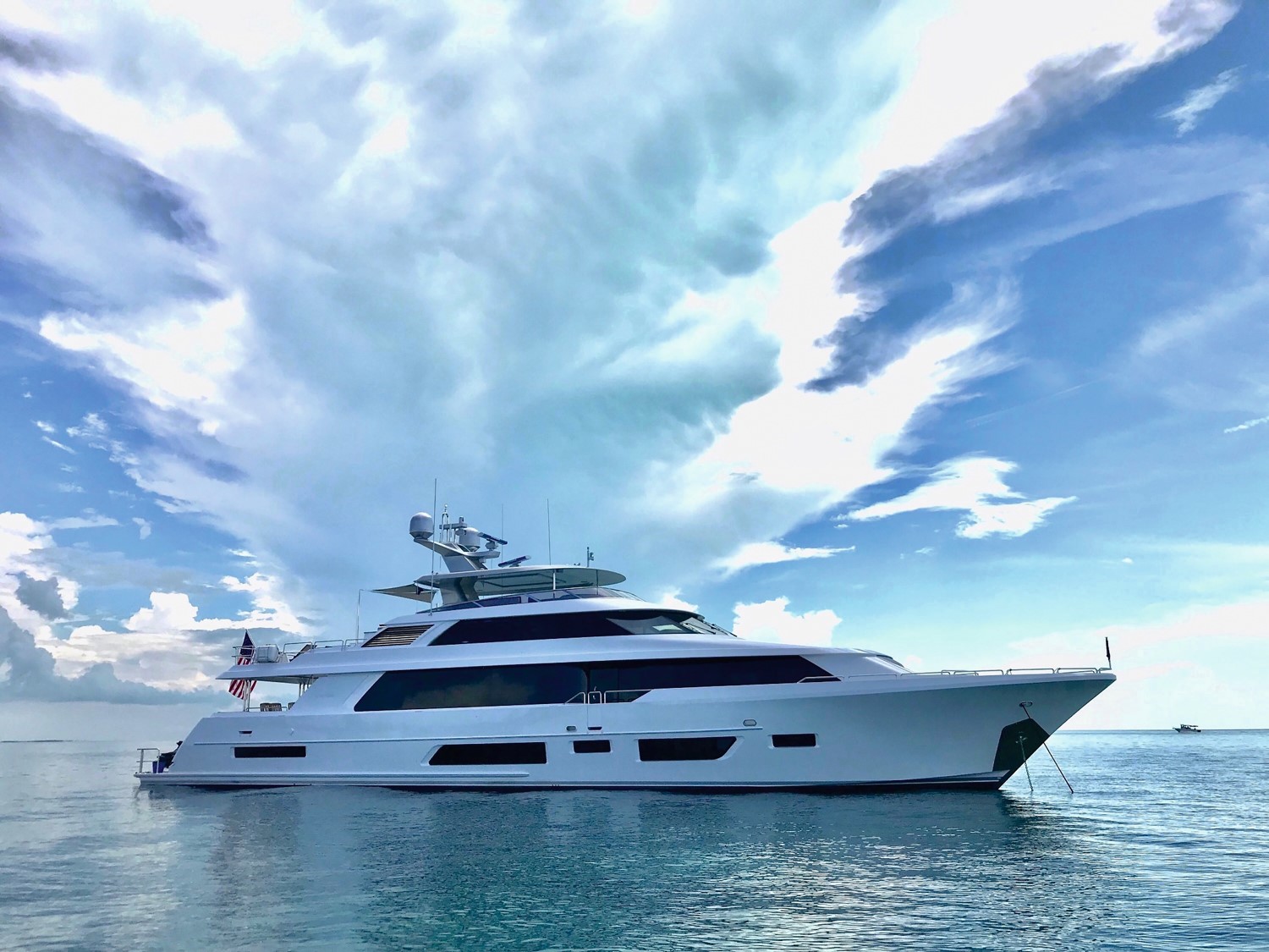 A sleek white yacht sails on calm blue waters under a partly cloudy sky.