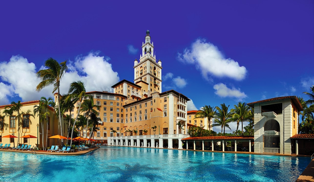 Historic hotel with a tower by a blue pool under a clear sky.