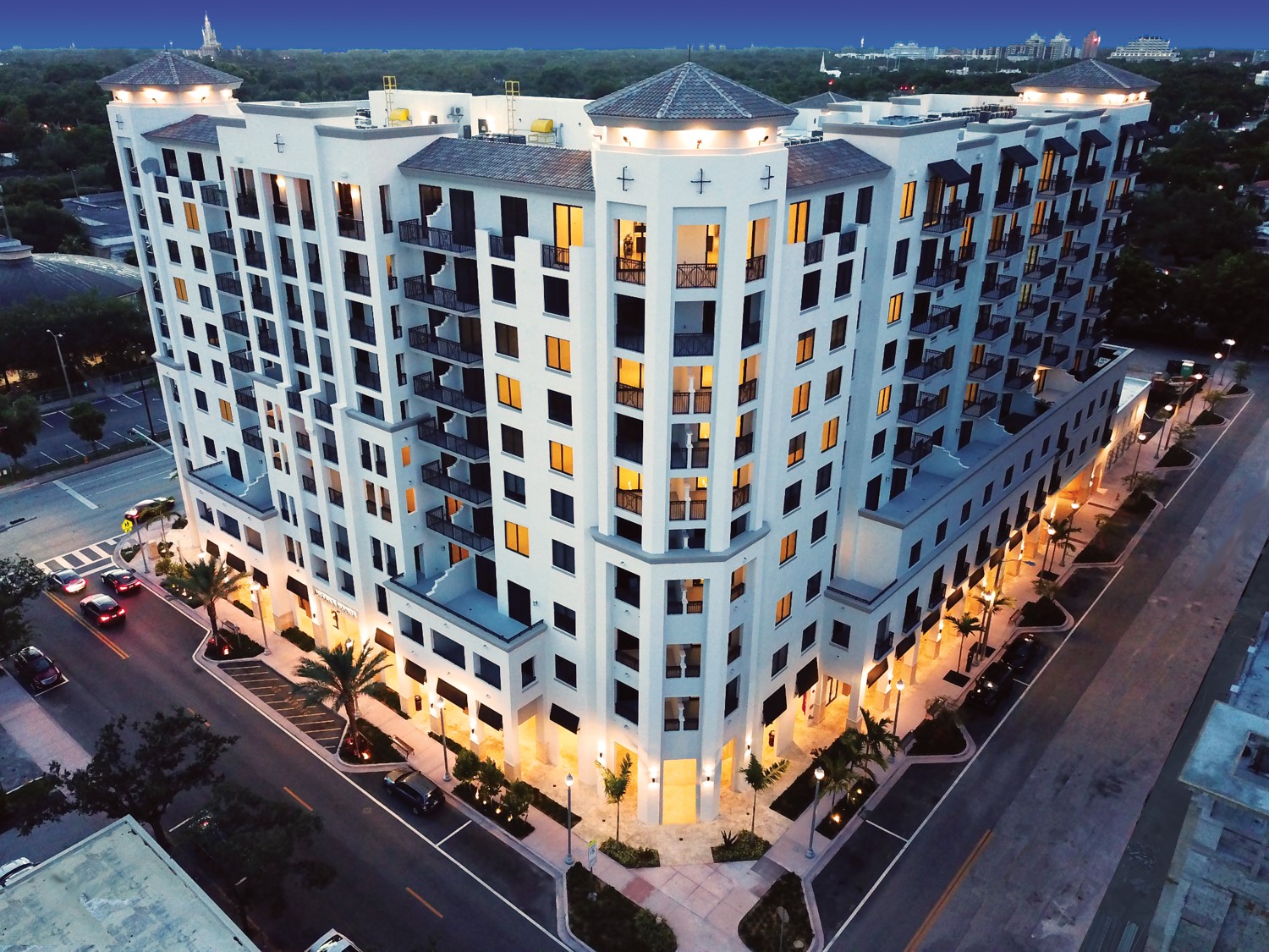 Modern residential building illuminated at dusk on a city corner.