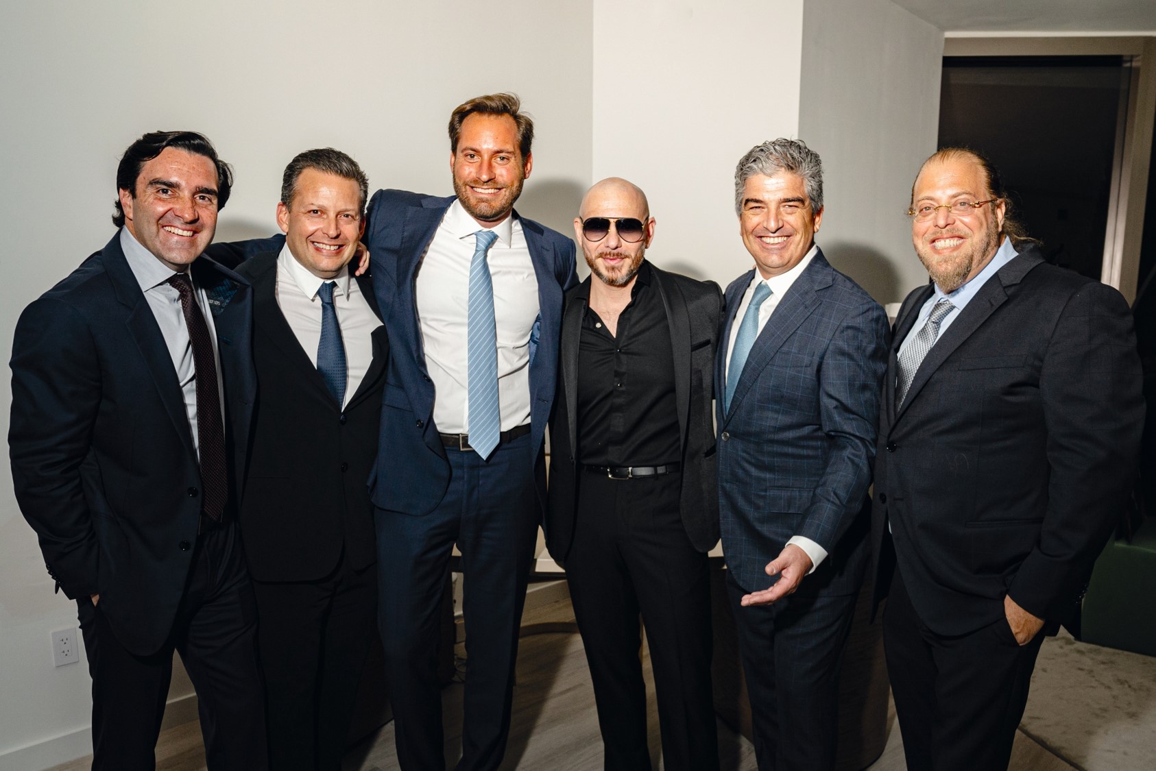 Group of men in suits and sunglasses posing together indoors.