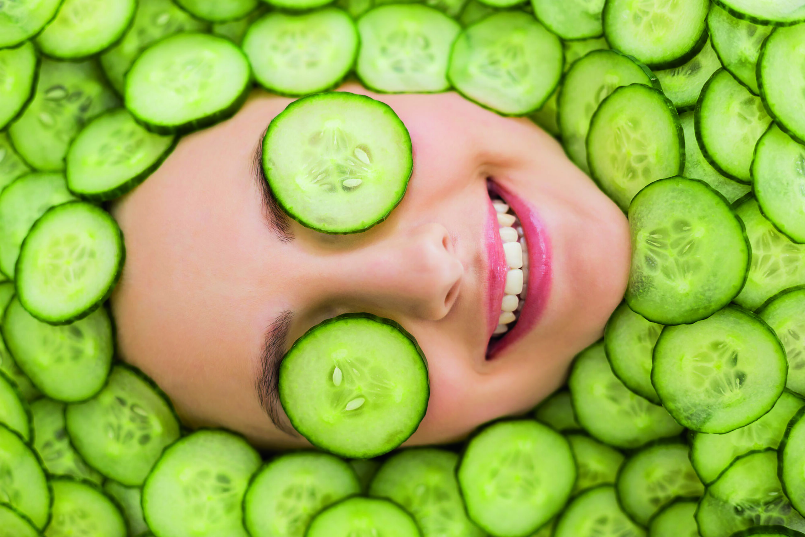 A woman with cucumber slices on her face surrounded by cucumber slices.