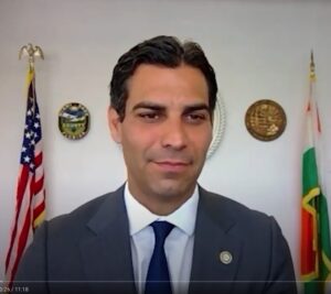 Man in formal suit with American flag and official emblems in background.