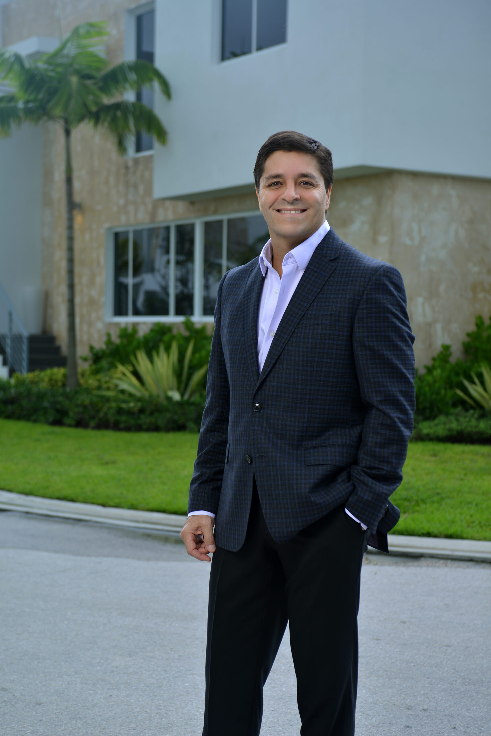 Man in a dark suit standing outdoors, smiling at the camera.