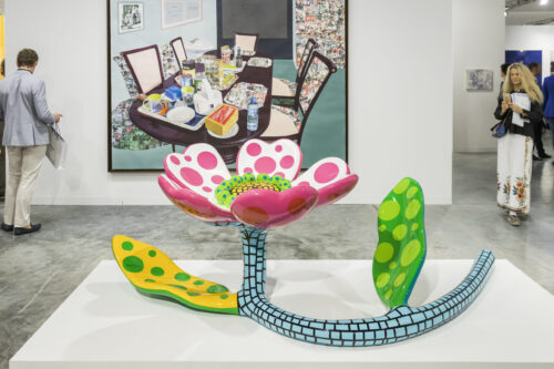 Colorful sculpture of a flower with pink petals and green leaves indoors.