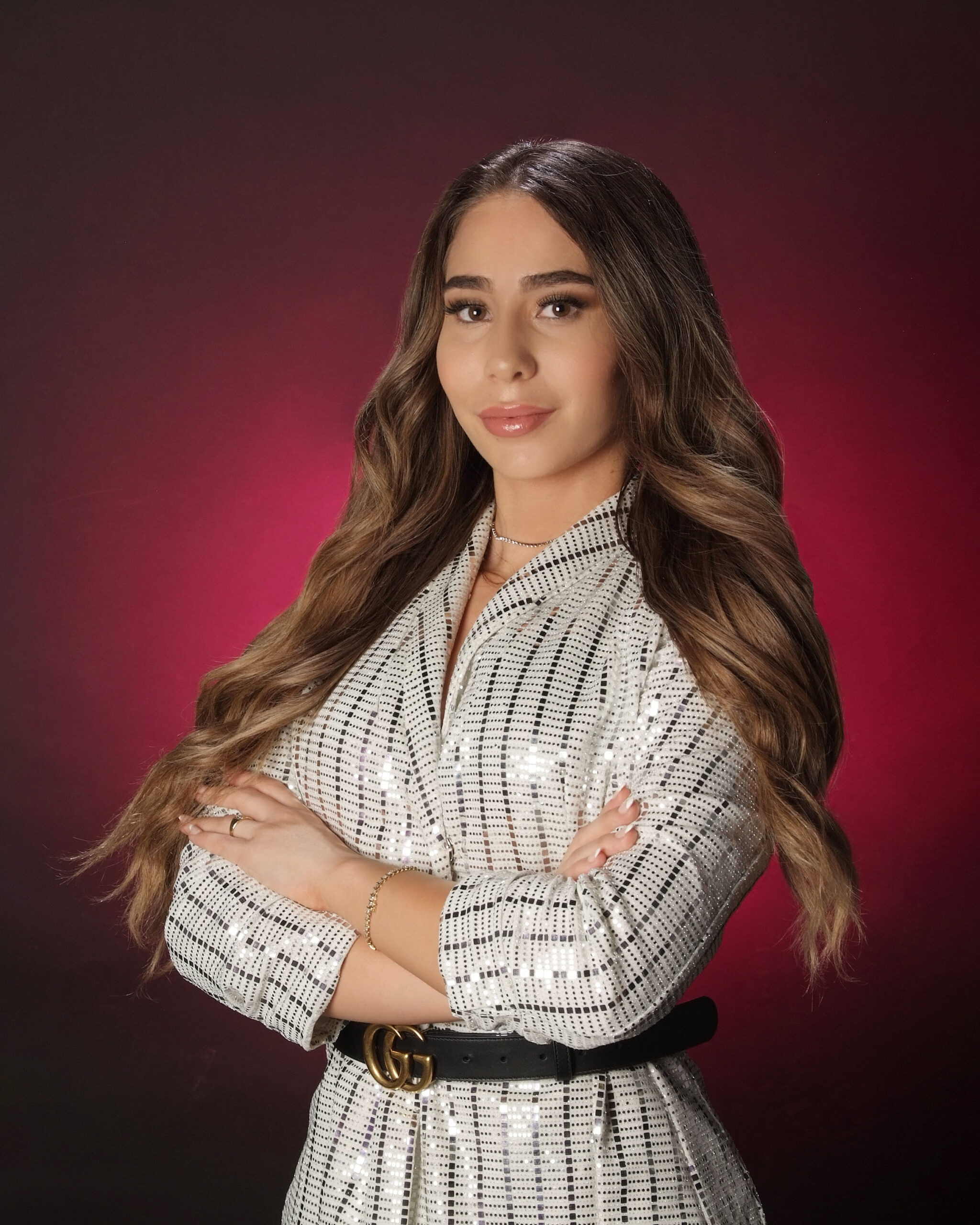 Confident young woman with long hair poses against a red background.