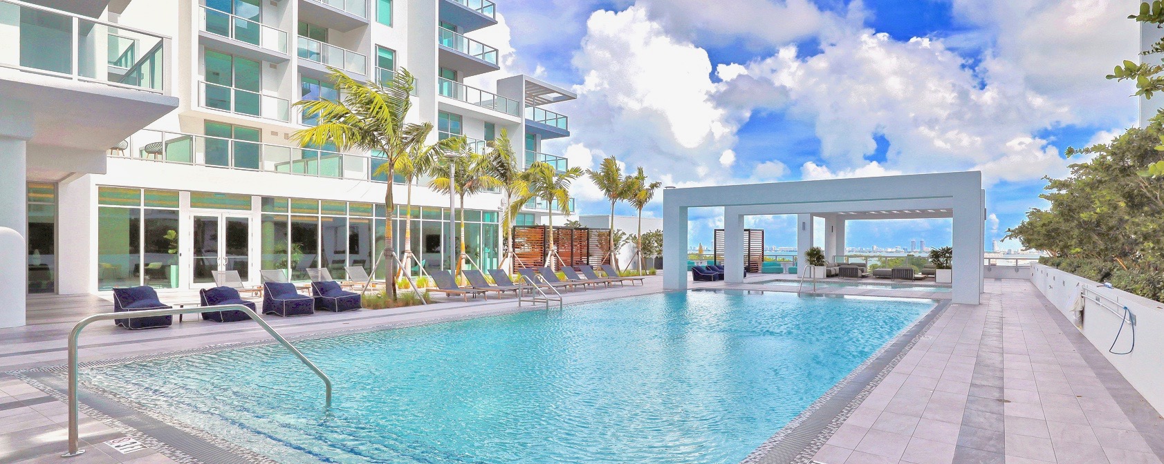 Modern pool area with palm trees and clear blue sky.