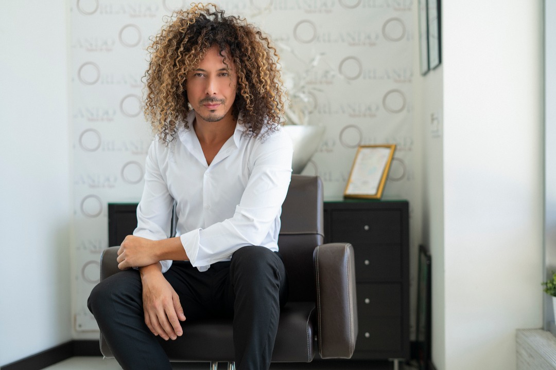 Man with curly hair sitting confidently in a modern room.