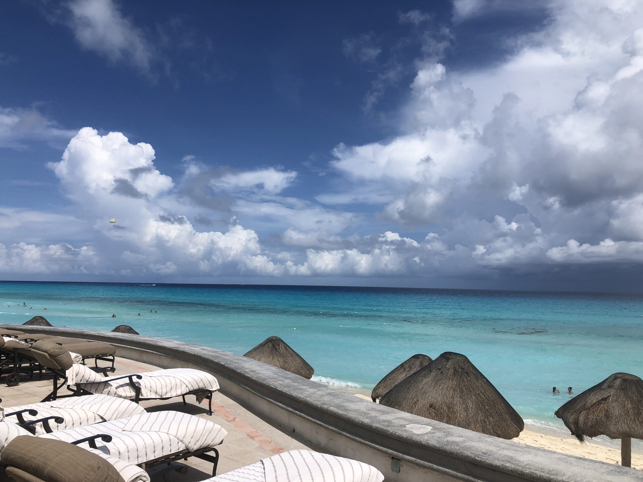 Beach chairs overlooking clear turquoise ocean and cloudy sky.