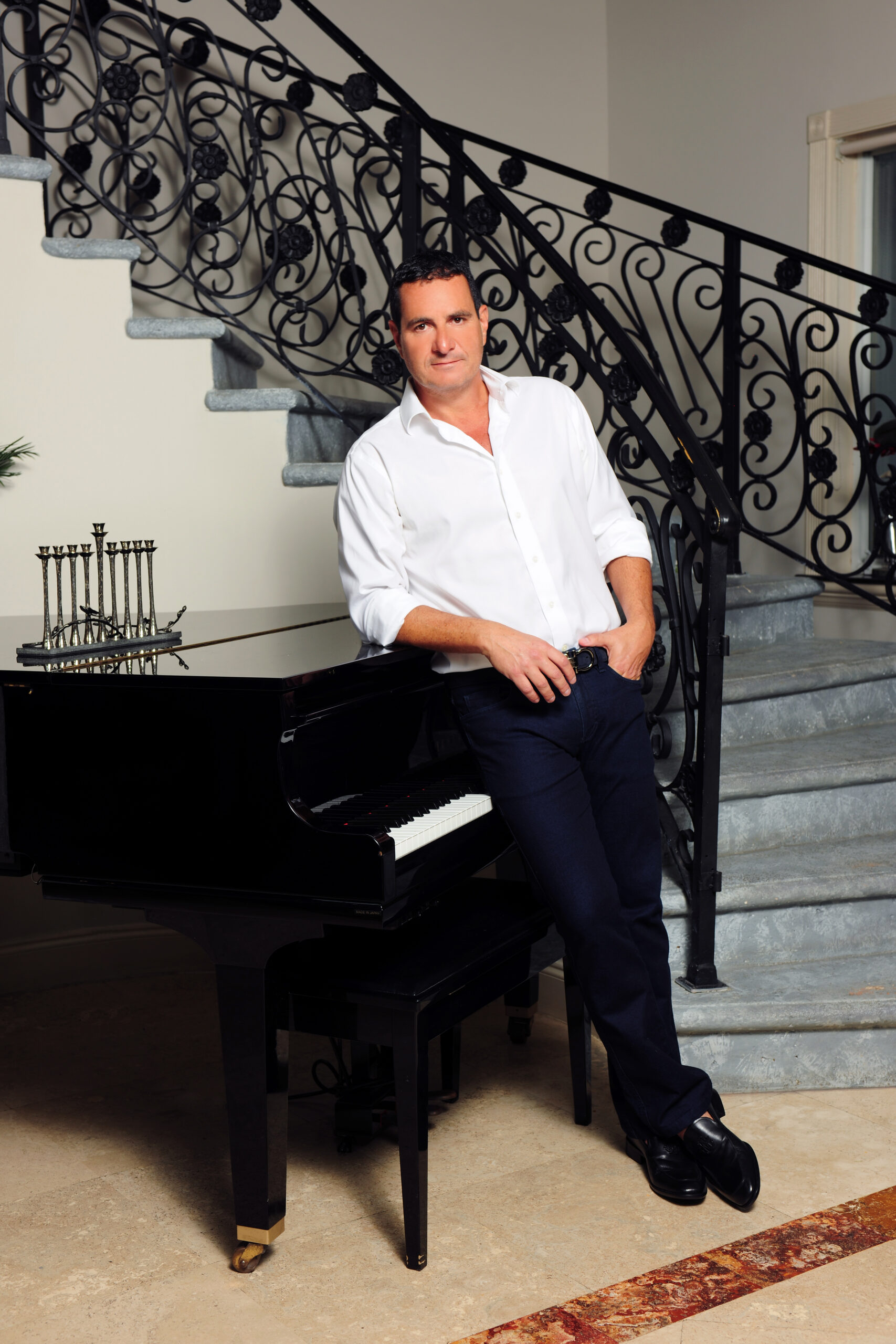 Man in white shirt posing by staircase with ornate railing.