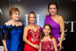 Four females dressed elegantly in vibrant evening gowns, smiling for a photo.