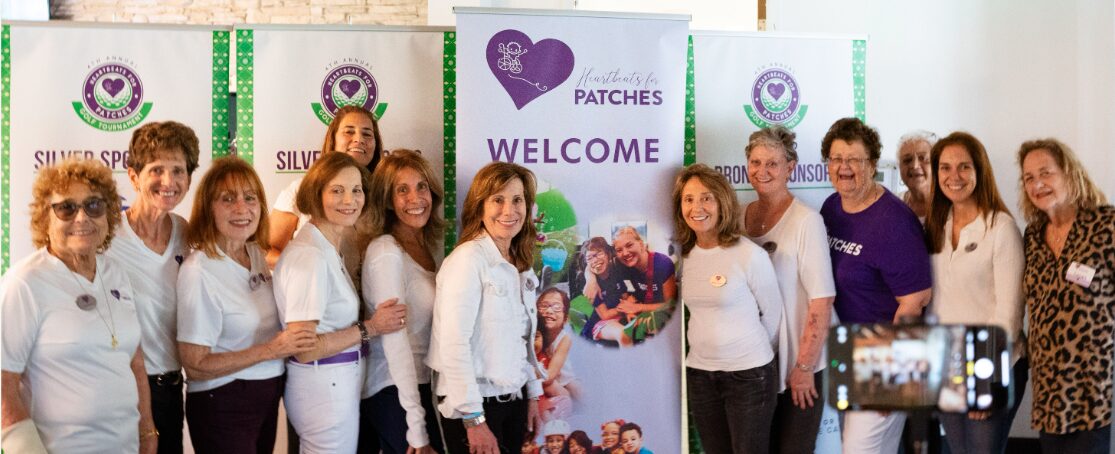 Group of women standing together in front of a welcome banner for a patch event.