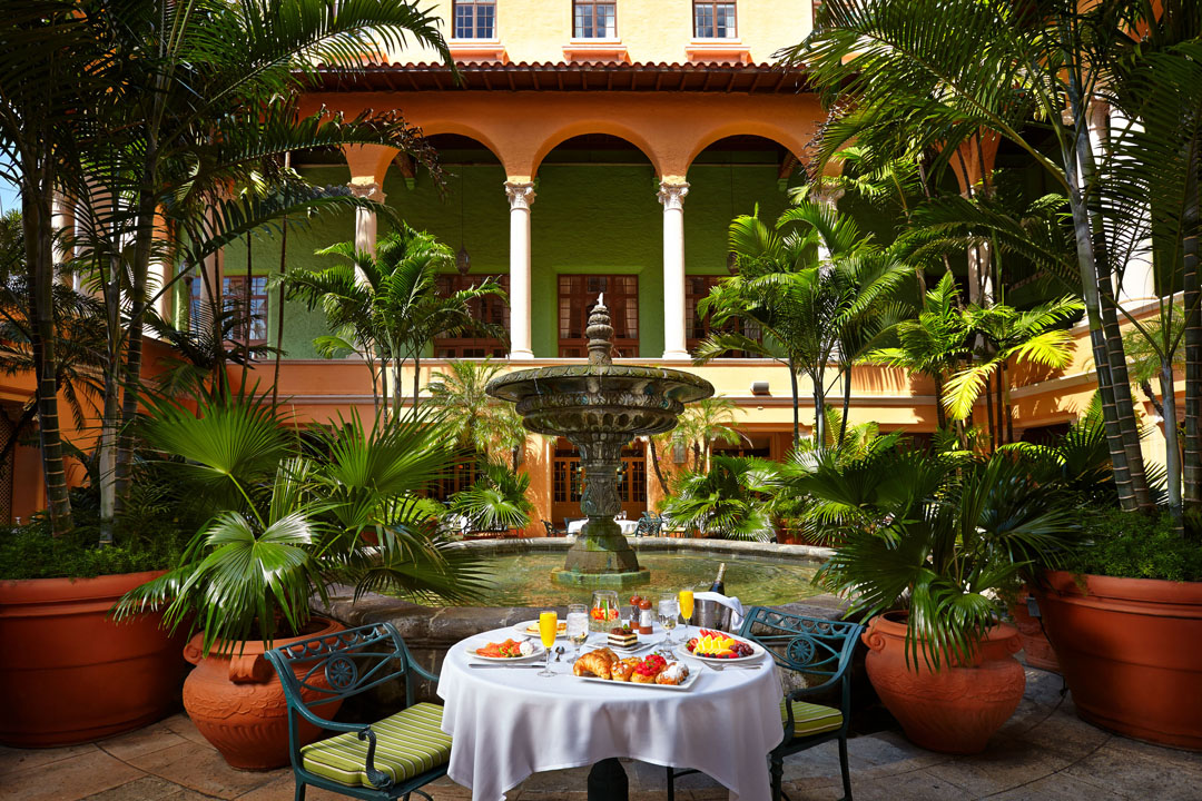 Elegant outdoor dining setup in a lush garden courtyard with tropical plants.