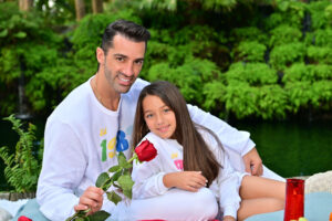 Man and young girl holding a rose, smiling outdoors.