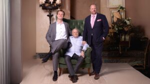 Three men dressed formally, posing indoors with a green armchair.
