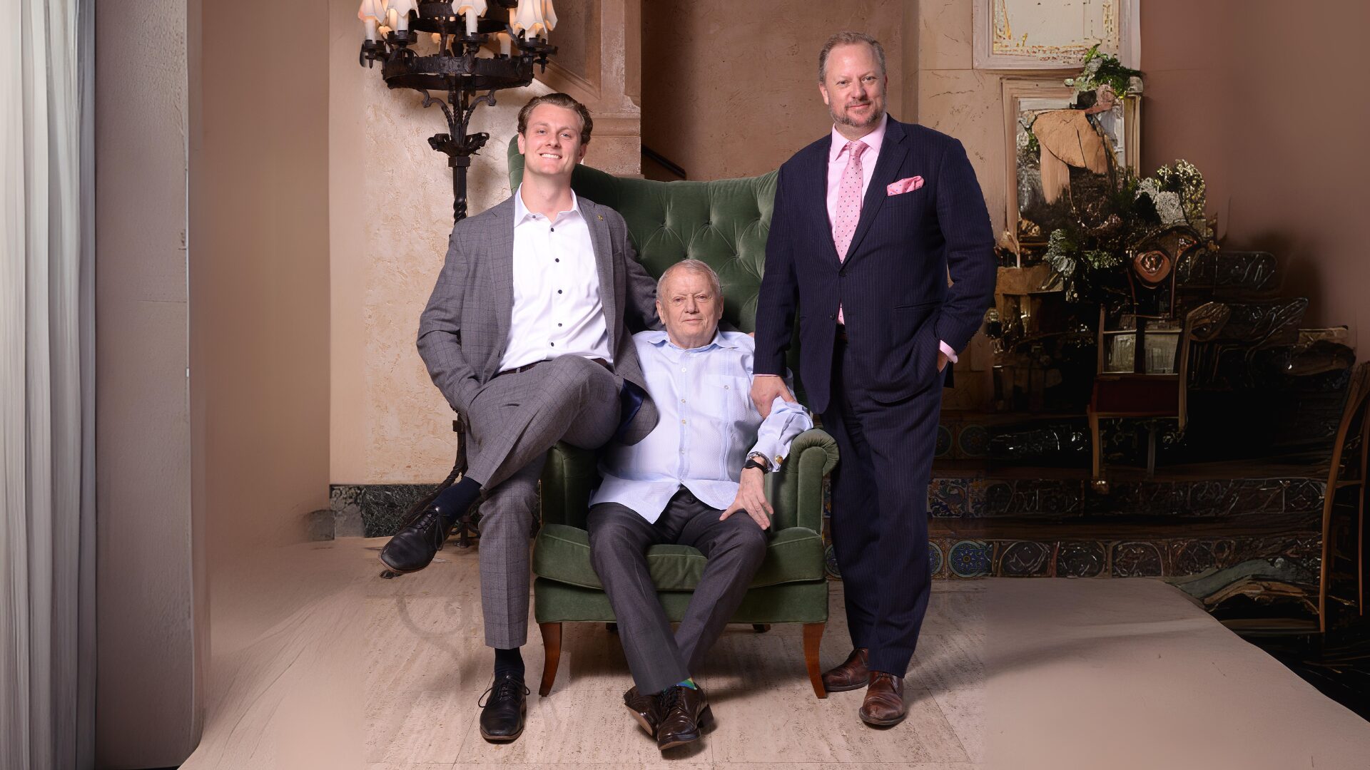 Three men dressed formally, posing indoors with a green armchair.