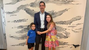 Man posing with two young girls in front of a textured wall.