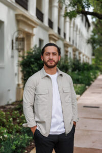 Man standing outdoors in a casual light jacket and white shirt.