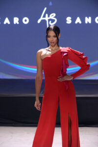 Model in a striking red one-shoulder jumpsuit on runway.