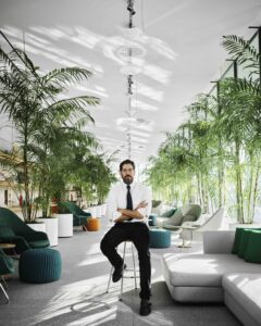 Man sitting confidently on a chair in a modern, plant-filled office space.