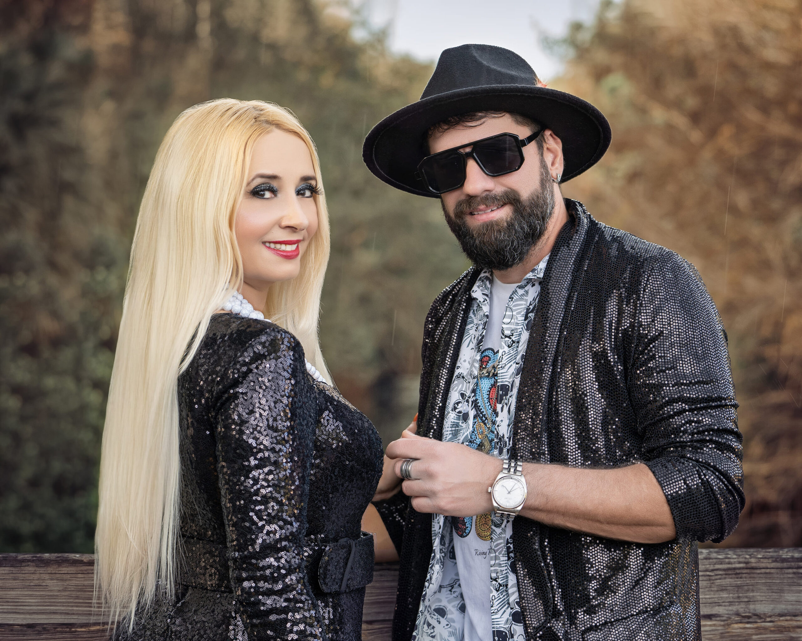 A stylish couple poses outdoors, both wearing dark velvet jackets.