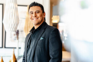 Smiling man in a black suit jacket posing indoors with warm lighting.