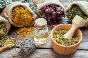 Various dried herbs, essential oil, and a wooden mortar with pestle on a table.
