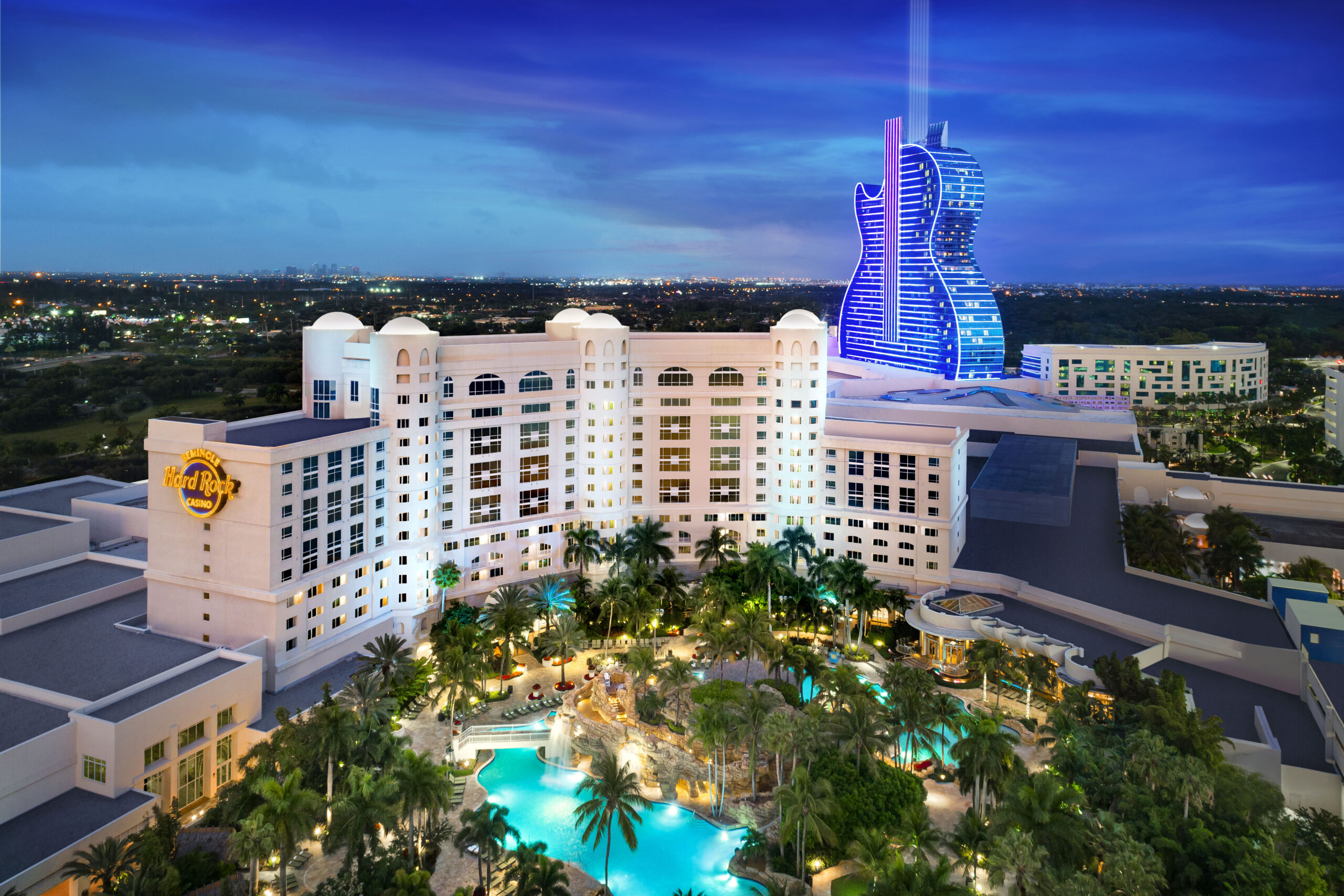 Luxurious hotel with illuminated pool and unique guitar-shaped building at night.