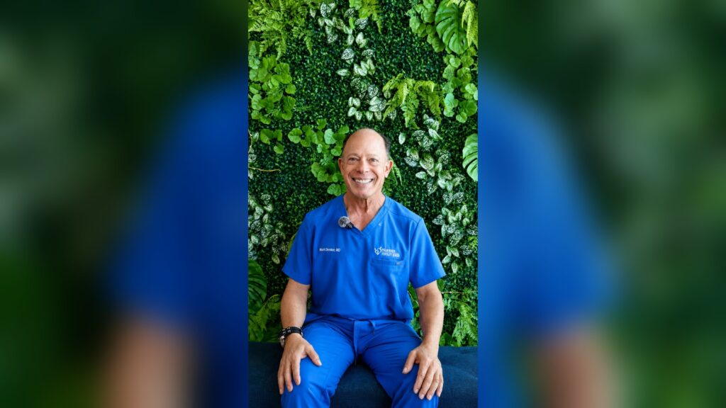Dr. Mark S. Denker, reproductive endocrinologist, seated in front of a green plant wall