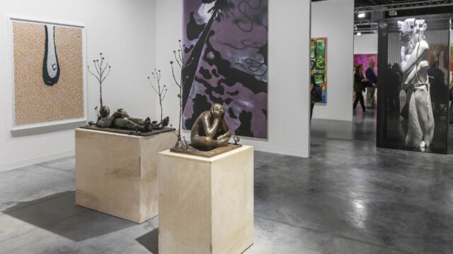Sculptures displayed on pedestals in an art gallery with abstract paintings in the background.