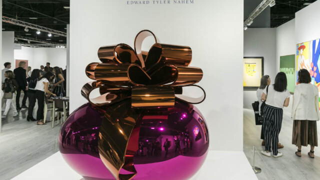 Shiny pink vase with large metallic gold bow on top in gallery.