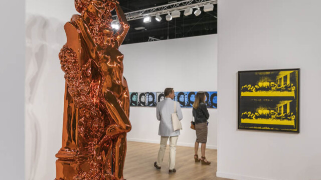 Visitors explore a modern art gallery with sculptures and digital displays.