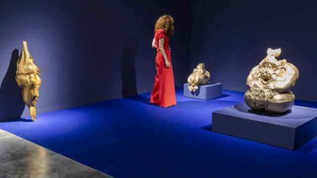 Woman in a red dress viewing sculptures in a dimly lit gallery.