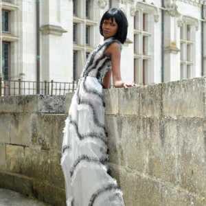 Woman in a stylish monochrome dress leaning on a stone wall outdoors.
