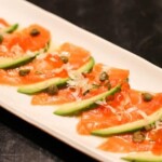 Appetizer with smoked salmon, avocado slices, and a drizzle of sauce on a white plate.
