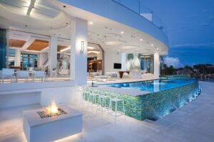 Modern luxury poolside patio with fire pit and bar seating.